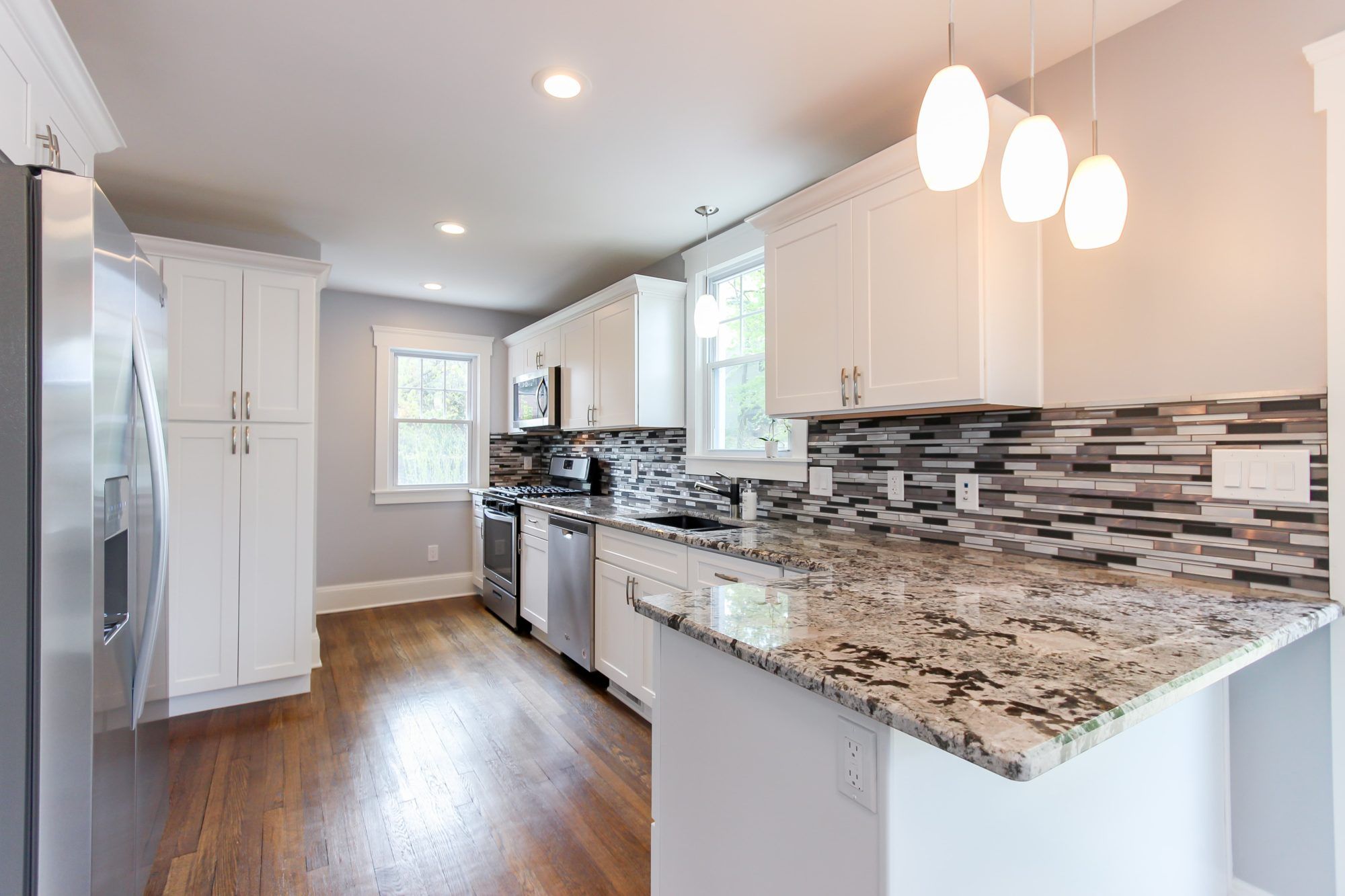 White kitchen cabinetry, stone countertops, pendant lighting, and a warm wood floor.